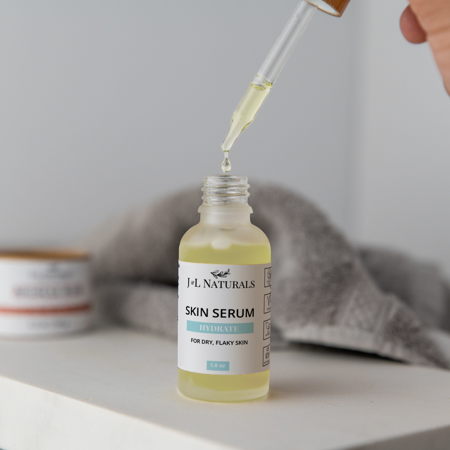 Skin Serum Duo bottle with dropper dispensing hydrating serum for dry, flaky skin on white surface with blurred towel background